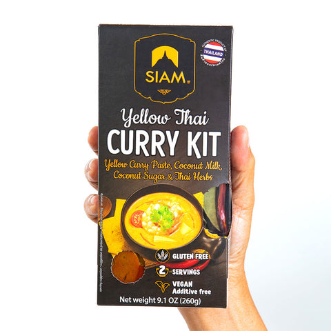 Hand holding a Siam Yellow Thai Curry Kit packaging on a white background